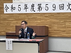 テーブルを前にマイクを持って話をする佐藤広行氏