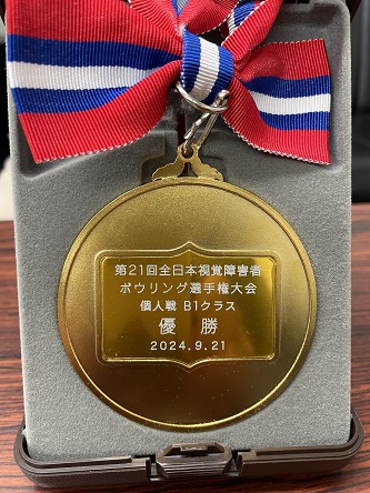 「第21回全日本視覚障害者ボウリング選手権大会個人戦B1クラス優勝、2024.9.21」と表面に白文字で書かれた優勝メダル