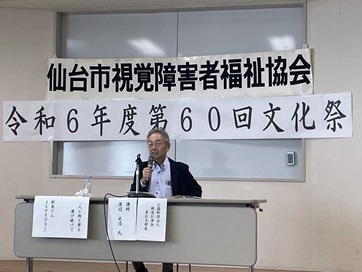 テーブルを前にマイクを持って話をする渡辺光浩氏