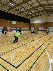 手前のコートからサーブを打つ選手、ネットの向こうに前衛3選手がブロック態勢をとっている